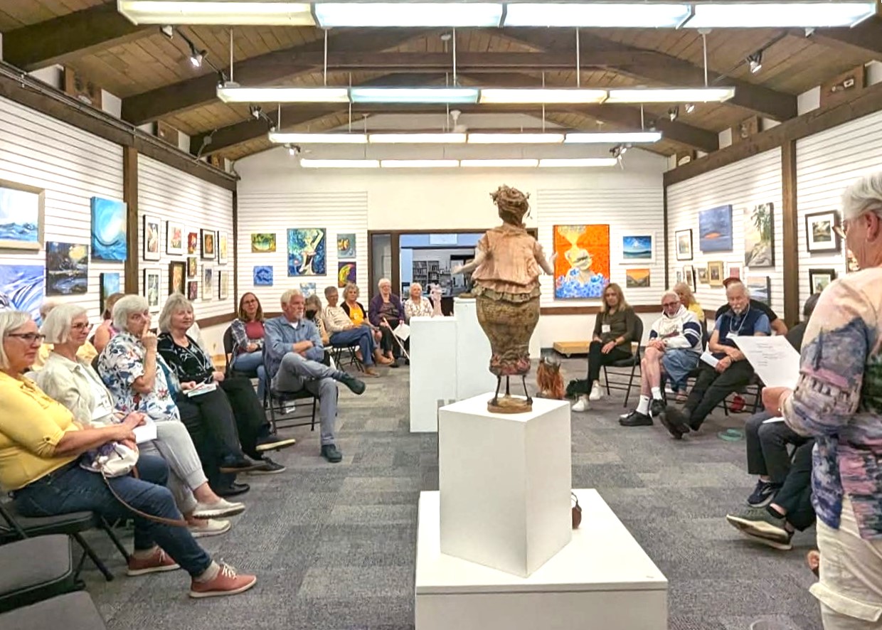Group of people seated in a gallery for a meeting surrounded by displayed artwork.